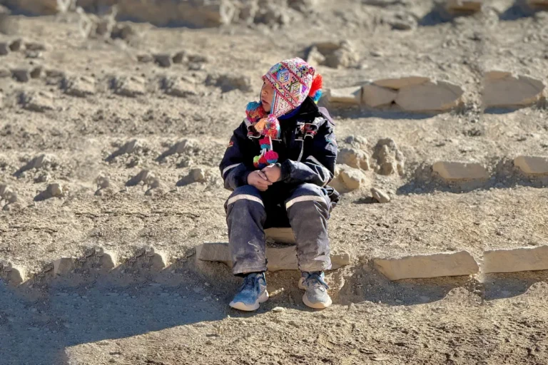 Child wearing a colorful Andean chullo, seated among rocks in the Peruvian highlands